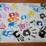 Zdjęcie prezentuje odbite dłonie nowych mieszkańców w różnych kolorach z podpisanymi imionami.