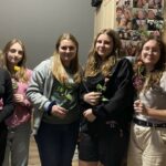 Pięć dziewczyn uśmiecha się do zdjęcia, stoją i trzymają w rękach róże.