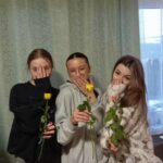 Trzy dziewczyny stoją, zakrywają dłońmi usta, trzymają w rękach róże.